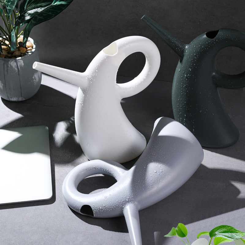 Green household vegetable watering kettle with long spout pouring water in garden