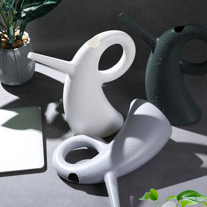 Green household vegetable watering kettle with long spout pouring water in garden